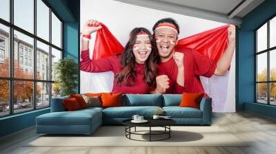 A young Asian couple with a happy successful expression wearing red top and headband while holding Indonesia's flag, isolated by white background. Indonesia's independence day concept. Wall mural