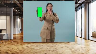 Shocked government worker woman wearing khaki uniform and glasses presenting copy space on phone. Wall mural