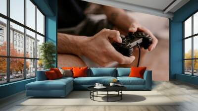 Hipster man plays video games on a couch. Relaxing time. Fun weekend. Concentrated on a video game. Winning the game, gambling. Multiplayer game. Online gaming. Streaming video game. Soccer, racing Wall mural