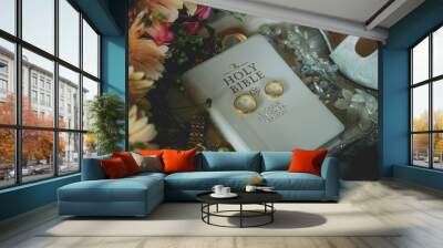 Closeup shot of a pair of golden wedding rings on a white Bible on a table with accessories Wall mural