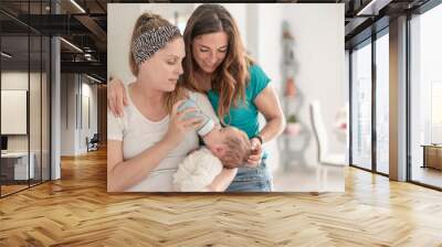 A lesbian couple giving a bottle of milk to their baby, gay marriage, gay parents and adoption concept Wall mural