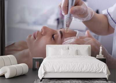 close up of Cosmetologist,beautician applying facial dermapen treatment on face of young woman customer in beauty salon.Cosmetology and professional skin care, face rejuvenation. Wall mural