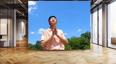 Young asian man praying and meditating in a outdoor park with blue sky and clouds Wall mural