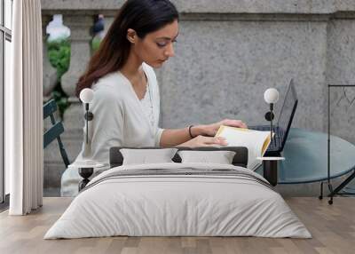 Young attractive woman reading while sitting outside in urban park Wall mural