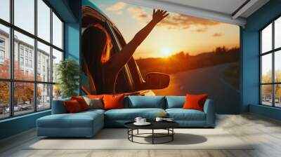 Woman enjoying road trip waving from car window at sunset Wall mural