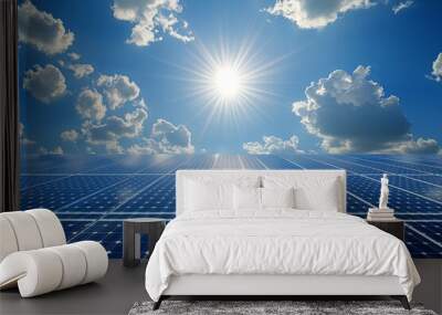 A vast solar panel field under a bright blue sky with fluffy white clouds and the sun shining brightly. Wall mural