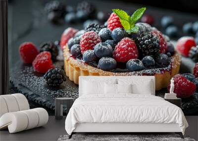 A luxurious fruit tart topped with an array of fresh berries, including raspberries, blueberries, and blackberries, dusted with powdered sugar and garnished with a mint leaf, on a dark slate plate. Wall mural