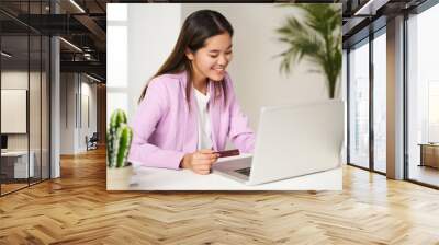 Young asian woman making online purchases with credit card payment from the coworking computer Wall mural