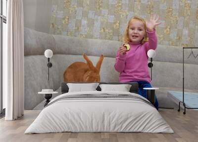 little girl with a rabbit eating apples,a child eats apples with a rabbit in the room, plays with a rabbit on the sofa Wall mural