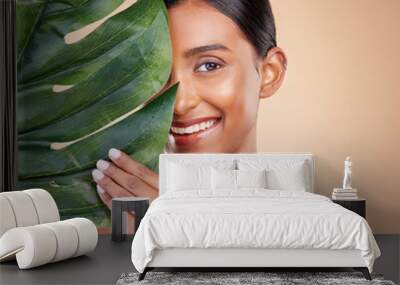 Portrait, facial and palm leaf with a model woman in studio on a beige background for natural skincare. Beauty, face and nature with an attractive young female posing for cosmetics or luxury wellness Wall mural