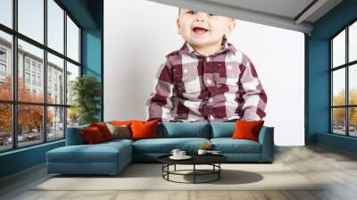 a cute 1 year old baby sits in white studio with jeans and a red white flannel looking and laughing looking above camera Wall mural