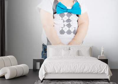 a cute 1 year old stands in a white studio setting. The boy has a intent expression. He is dressed in Tshirt, jeans, suspenders and blue bow tie Wall mural