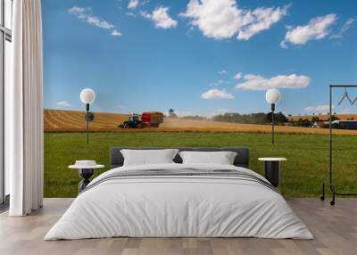 Harvesting. A tractor collecting wheat on a field. Wall mural