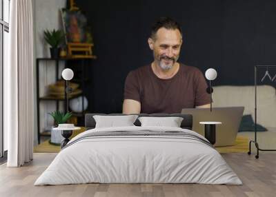 Portrait of middle-age man sitting at his desk in the home office working on laptop and dreanking coffee Wall mural