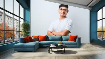 Portrait of young handsome Asian man wearing casual shirt and glasses standing with arms crossed and smiling at camera Wall mural