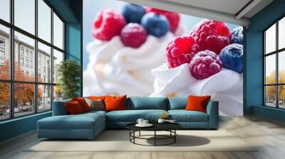 Two delicate meringue desserts topped with fresh raspberries and blueberries, with a few berries scattered around, against a softly blurred background of blue and white bokeh. Wall mural