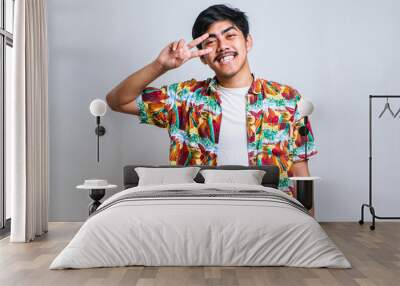 Young handsome asian guy wearing casual shirt doing peace symbol with fingers over face Wall mural