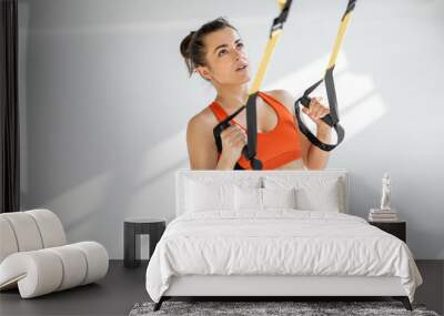 Athletic woman in bright sportswear doing cardio training on suspension straps at white gym. TRX training on fitness straps Wall mural