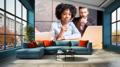 Beautiful african woman with handsome caucasian man working with laptop at the modern office interior Wall mural