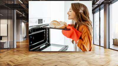 Beautiful young woman baking bread in the oven at the modern white kitchen at home Wall mural