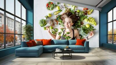 Beauty portrait of a sports woman surrounded by various healthy food lying on the floor. Healthy eating and sports lifestyle concept Wall mural