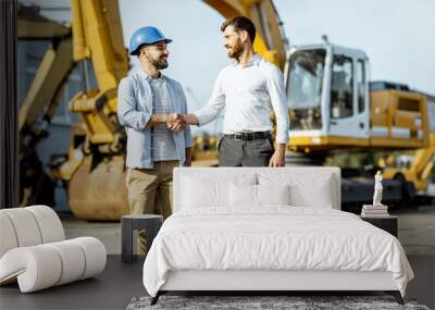 Builder choosing heavy machinery for construction, talking with a sales consultant on the open ground of a shop with special vehicles Wall mural