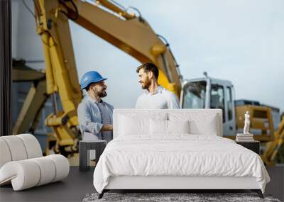 Builder choosing heavy machinery for construction, talking with a sales consultant on the open ground of a shop with special vehicles Wall mural