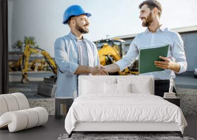 Builder choosing heavy machinery for construction with a sales consultant shaking hands on the open ground of a shop with special vehicles Wall mural