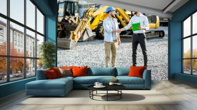 Builder choosing heavy machinery for construction with a sales consultant shaking hands on the open ground of a shop with special vehicles Wall mural