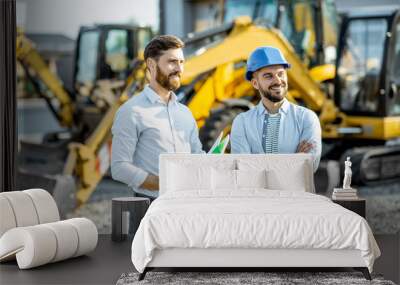 Builder choosing heavy machinery for construction with a sales consultant standing with some documents on the open ground of a shop with special vehicles Wall mural