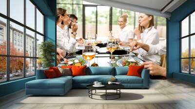 Business people dressed in white shirts having fun sitting together during a business lunch with delicious meals and wine in the modern restaurant Wall mural