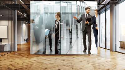 Business people walking in the hallway of the modern office building with employees working behind glass partitions. Work in a large business corporation Wall mural