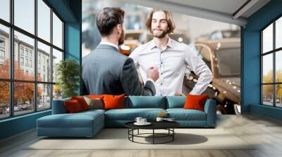 Car salesman helping a young male client to make a decision talking together at the showroom with luxury cars Wall mural