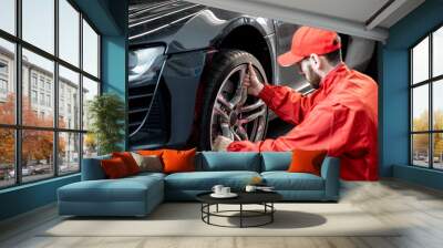 Car service worker in red uniform changing wheel of a sport car at the tire mounting service Wall mural