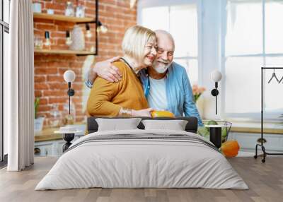 Cheerful senior couple cooking food with healthy fresh ingredients on the kitchen at home. Concept of healthy nutrition in older age Wall mural