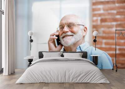 Cheerful senior grandfather talking with phone near the window at home Wall mural