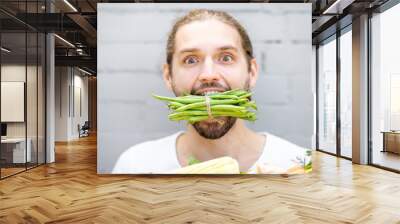 Close portrait of a handsome man biting green beans on the brick wall background Wall mural