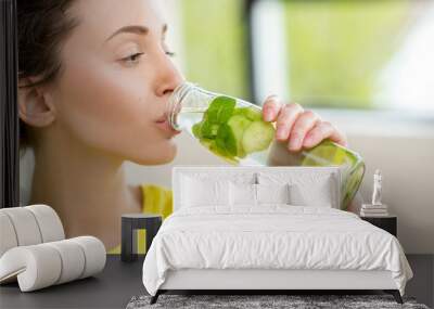 Close-up of a woman drinking water with mint, cucumber and lime during a workout with dumbbells. Detox dieting concept Wall mural