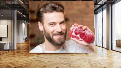 Close-up portrait of a handsome man with raw meat steak on the kitchen Wall mural