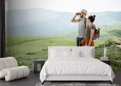 Couple enjoying beautiful landscape views, while traveling with backpacks in the mountains during the summer vacations Wall mural