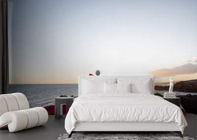 Couple enjoying beautiful views on the ocean, hugging together near the car on the rocky coast, wide view from the side with copy space on the sky Wall mural