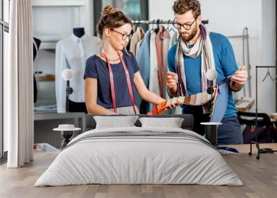 Couple of fashion designers choosing fabric standing at the studio full of tailoring tools and equipment Wall mural