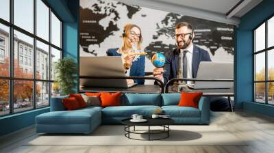 couple of travel managers playing with globe and airplane sitting at the agency office with world ma Wall mural