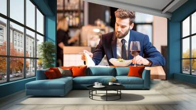 Elegant businessman dressed in the suit having a dinner with salad and wine sitting at the modern restaurant interior Wall mural