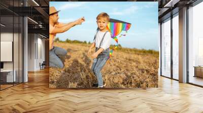 Father with son launching colorful air kite on the field. Concept of a happy family having fun during the summer activity Wall mural