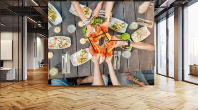 Friends clinking glasses with cocktail drinks, top view on the table full of snacks outdoors Wall mural