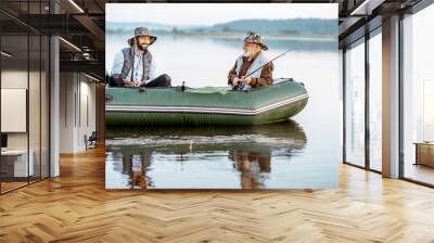 Grandfather with adult son fishing on the inflatable boat on the lake early in the morning Wall mural