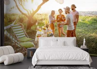 Group of a young and happy friends having fun during a festive picnic in the beautifully decorated garden with lunch table on a sunset Wall mural