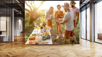 Group of a young and happy friends having fun during a festive picnic in the beautifully decorated garden with lunch table on a sunset Wall mural