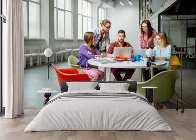 Group of a young coworkers dressed casually working together with laptops in the modern office Wall mural